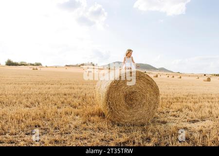 Fille joueuse assise sur la balle de paille dans le champ de chaume sur la journée ensoleillée Banque D'Images
