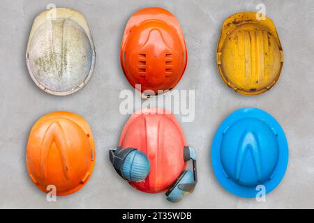 Six casques de construction vieux et usés colorés accrochés à un mur de béton Banque D'Images