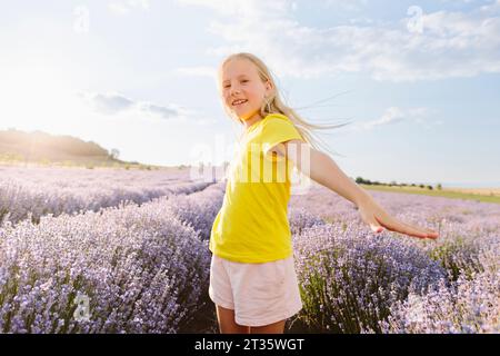 Fille heureuse avec les bras tendus debout dans le champ de lavande sous le ciel Banque D'Images