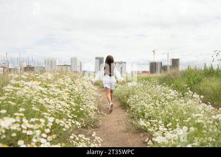 Fille insouciante courant au milieu des plantes de Marguerite dans la prairie Banque D'Images