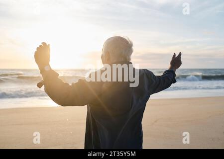 Homme âgé avec les bras levés debout devant la mer à la plage Banque D'Images