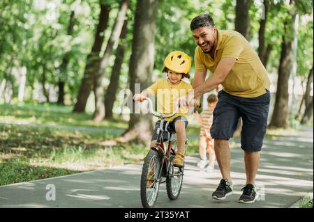 Heureux père aidant son fils à faire du vélo sur le sentier au parc Banque D'Images