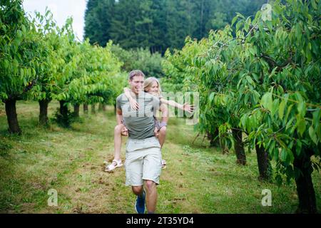 Père souriant donnant tour de piggyback à sa fille dans le jardin Banque D'Images