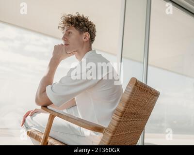 Homme contemplatif assis sur un fauteuil en bois à la maison Banque D'Images