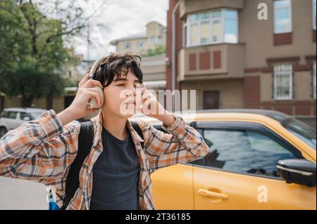 Adolescent écoutant de la musique à travers des écouteurs en ville Banque D'Images