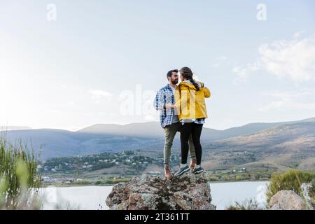 Couple affectueux debout ensemble sur le rocher en face de la montagne Banque D'Images