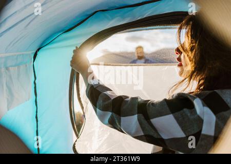 Jeune femme dézipping tente en vacances Banque D'Images