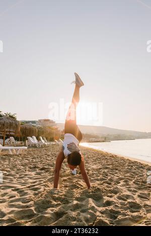 Femme pratiquant l'exercice d'étirement des jambes à la plage le jour ensoleillé Banque D'Images