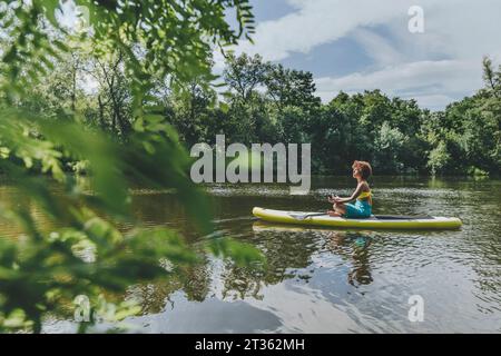 Jeune femme assise et méditant sur paddleboard dans le lac Banque D'Images