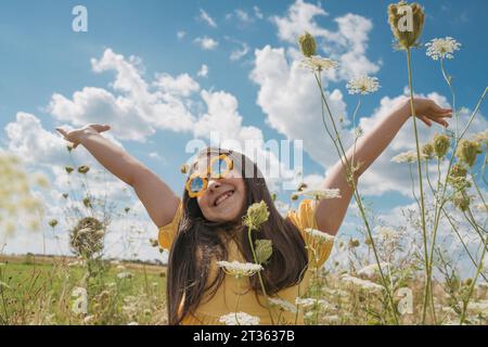 Fille heureuse avec les mains levées appréciant au champ de fleurs Banque D'Images