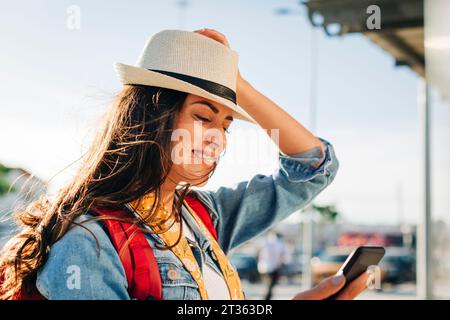 Heureuse jeune femme avec chapeau à l'aide du téléphone portable Banque D'Images
