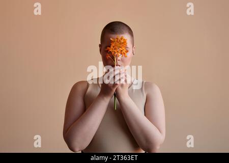 Femme couvrant le visage avec une fleur orange sur fond beige Banque D'Images