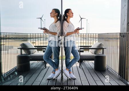 Portrait de jolie blonde appuyée sur un mur de verre avec modèle d'éolienne dans les mains Banque D'Images