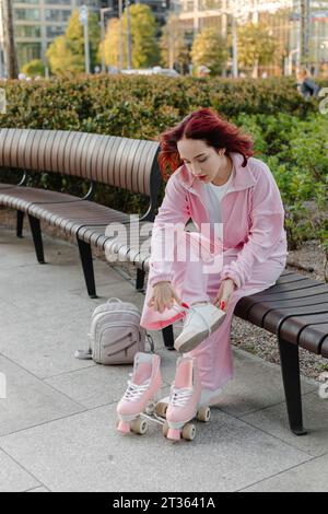 Femme attachant la dentelle de chaussure assise sur un banc avec des patins à roulettes Banque D'Images