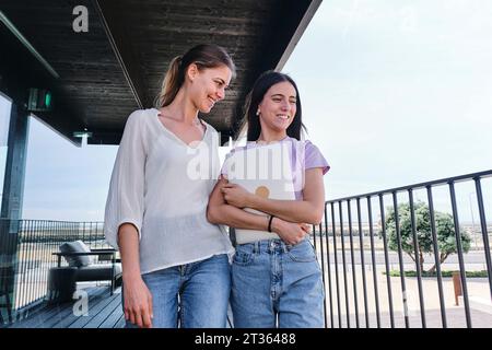 Deux jeunes femmes debout ensemble sur le balcon tenant un ordinateur portable Banque D'Images
