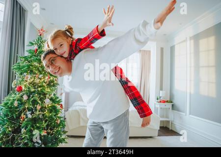 Père avec les bras tendus donnant un tour de gigyback à la fille à la maison Banque D'Images