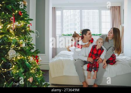 Famille assis sur le lit près de l'arbre de Noël à la maison Banque D'Images
