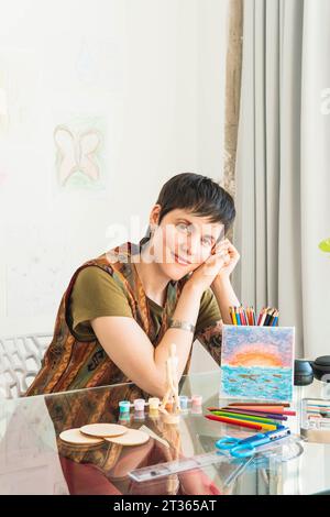 Artiste souriant assis avec la peinture à table Banque D'Images