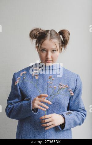 Adolescente portant un blazer bleu à l'envers et tenant des fleurs devant le mur Banque D'Images