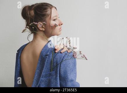 Adolescente portant blazer bleu à l'envers avec des fleurs dans la poche par le mur Banque D'Images