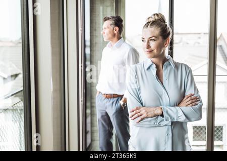 Femme d'affaires blonde souriante avec homme d'affaires debout en arrière-plan Banque D'Images