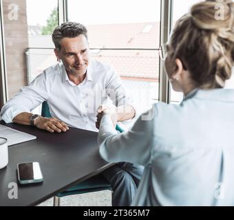 Homme d'affaires souriant serrant la main avec femme d'affaires au bureau Banque D'Images