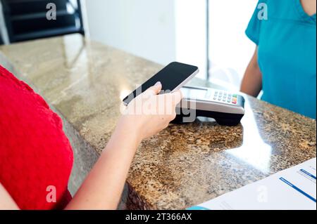 Patient payant par téléphone intelligent à la caisse dans le bureau du dentiste Banque D'Images