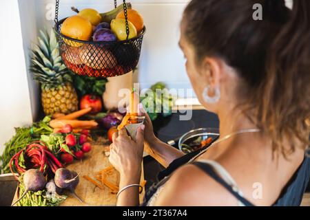 Femme épluchant la carotte dans la cuisine à la maison Banque D'Images