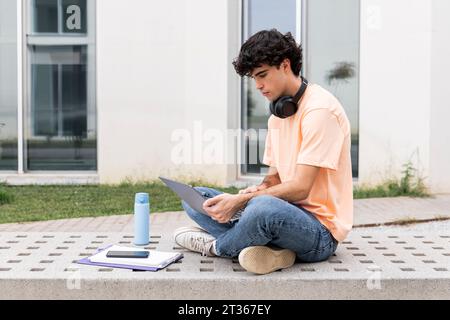 Jeune étudiant utilisant un ordinateur portable sur un banc en béton sur le campus Banque D'Images