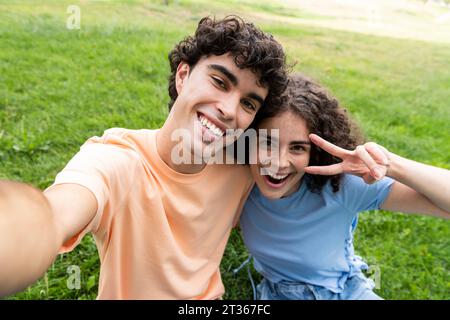 Heureux petit ami et petite amie prenant selfie sur l'herbe dans le parc Banque D'Images