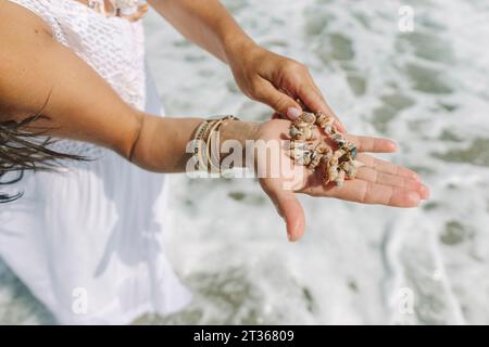 Femme tenant un bracelet fait de coquillages à la main près de la mer Banque D'Images