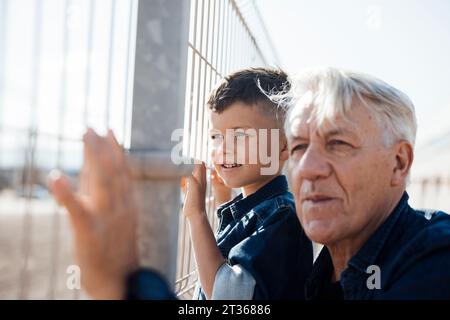 Garçon et homme senior regardant à travers la clôture Banque D'Images
