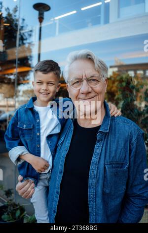 Homme aîné souriant avec petit-fils debout près du mur Banque D'Images