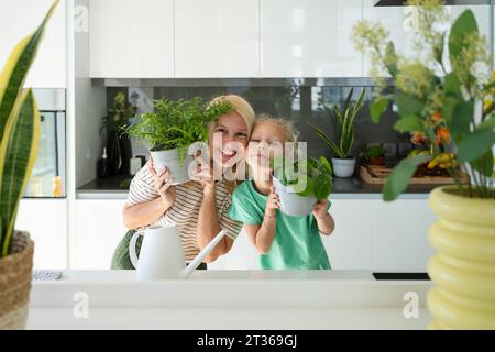 Mère et fille heureuses tenant des plantes dans la cuisine à la maison Banque D'Images