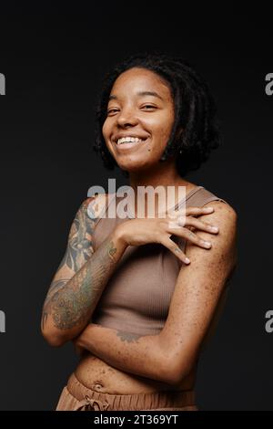 Femme heureuse avec des cicatrices d'acné et tatouage sur fond noir Banque D'Images