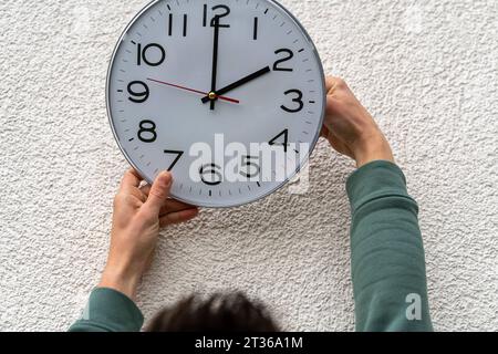 Augsbourg, Bavière, Allemagne - 17 octobre 2023 : l'homme fixe une horloge accrochée au mur à l'heure d'hiver. Concept de changement de temps *** Mann stellt eine an der Wand hängende Uhr UM auf Winterzeit. Zeitumstellung Konzept Banque D'Images