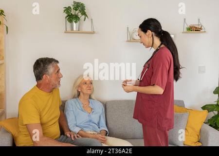 Soignant parlant à un couple mature assis sur un canapé à la maison Banque D'Images
