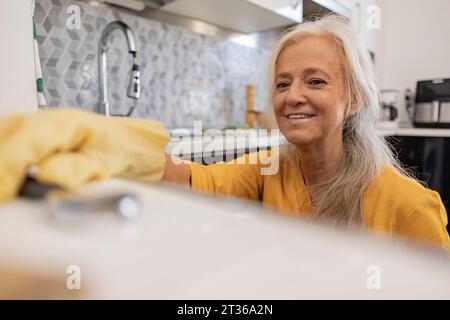 Homme mûr souriant faisant des corvées dans la cuisine à la maison Banque D'Images