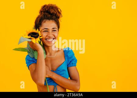 Heureuse jeune femme tenant le tournesol sur fond jaune Banque D'Images