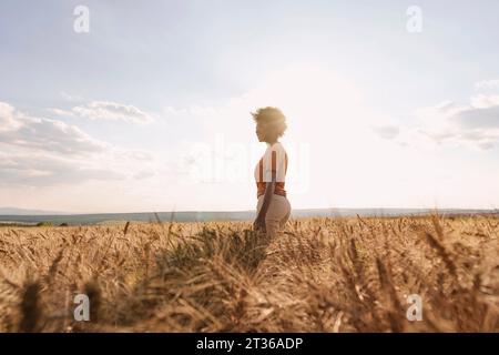 Jeune femme appréciant la solitude dans le champ d'orge au coucher du soleil Banque D'Images