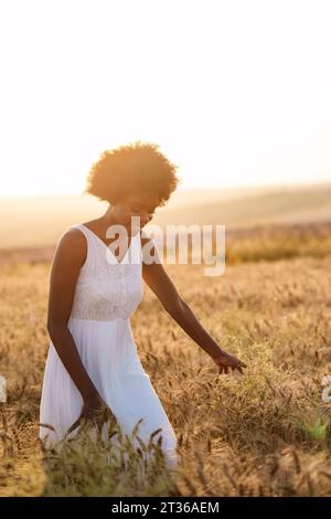 Femme heureuse marchant dans le champ de blé au coucher du soleil Banque D'Images