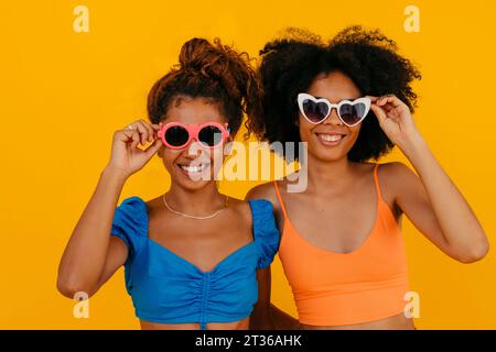 Femmes heureuses portant des lunettes de soleil sur fond jaune Banque D'Images