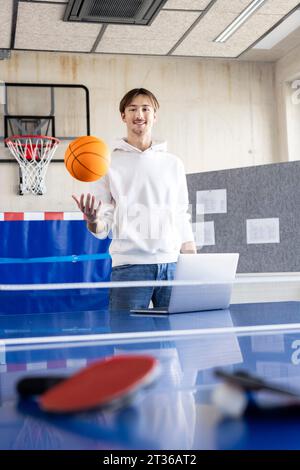 Homme d'affaires souriant debout avec basket-ball et ordinateur portable à la table de tennis Banque D'Images