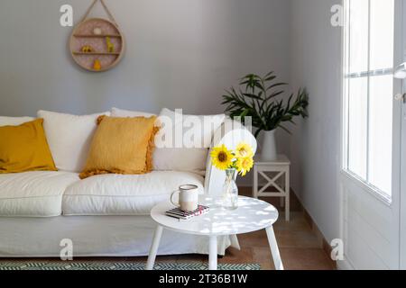 Salon avec canapé blanc, tournesols et tasse sur table à la maison Banque D'Images