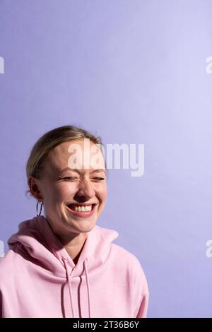 Femme souriant avec les yeux fermés sur fond violet en studio Banque D'Images