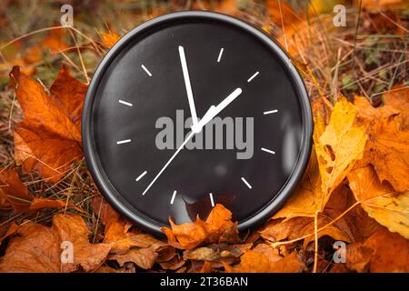 Gersthofen, Bavière, Allemagne. 23 octobre 2023. horloge ronde noire dans un tas avec des feuilles d'automne. Changement de temps en automne concept *** schwarze Runde Uhr in einem Haufen mit Herbstlaub. Zeitumstellung im Herbst Konzept crédit : Imago/Alamy Live News Banque D'Images