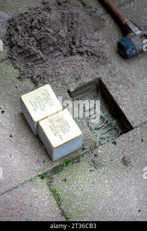 Wiesbaden, Allemagne - 17 octobre 2023 : un maçon pose Stolpersteine sur un trottoir dans le centre-ville de Wiesbaden, Allemagne. Un Stolperstein (littéralement « pierre d'achoppement ») est un cube de béton muni d'une plaque de laiton portant le nom et les dates de vie des victimes de l'extermination nazie. Banque D'Images