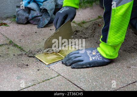 Wiesbaden, Allemagne - 17 octobre 2023 : un maçon pose Stolpersteine sur un trottoir dans le centre-ville de Wiesbaden, Allemagne. Un Stolperstein (littéralement « pierre d'achoppement ») est un cube de béton muni d'une plaque de laiton portant le nom et les dates de vie des victimes de l'extermination nazie. Banque D'Images