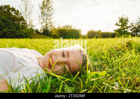 Garçon souriant allongé sur l'herbe au parc Banque D'Images