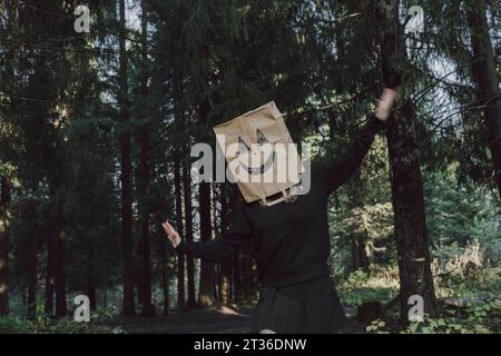 Femme insouciante portant un sac en papier sur le visage et dansant dans la forêt Banque D'Images